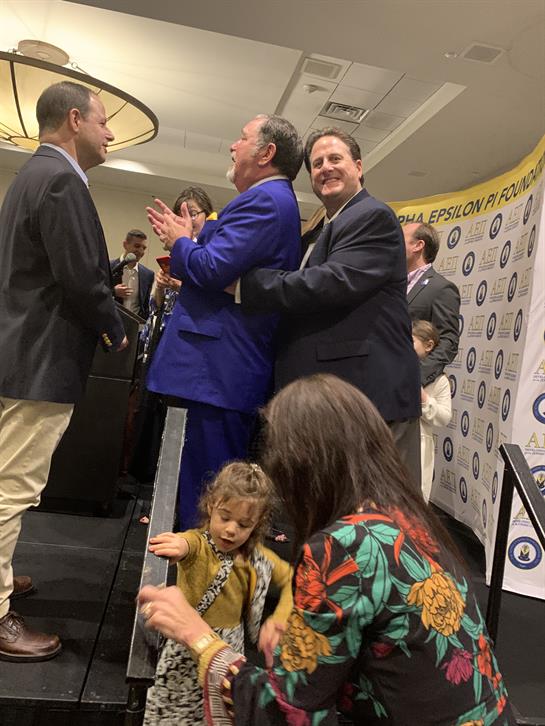 Guests celebrate an achievement at a formal event, applauding and interacting.