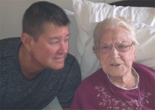 A younger man and an elderly woman share a caring conversation, smiling with warmth.
