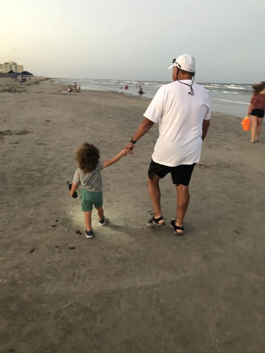A child and adult stroll along the beach, holding hands while enjoying the sunset view.