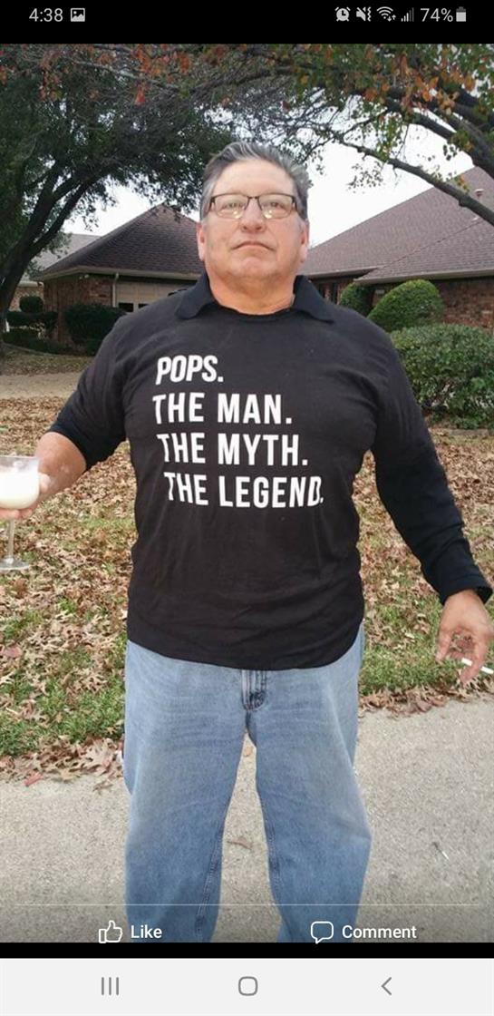 Man with a glass poses confidently outside a house, wearing a shirt that labels him as a legend.