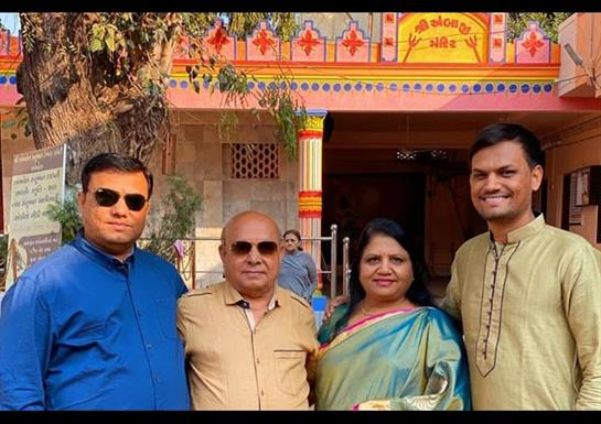 Four adults stand together smiling in front of a vibrant temple adorned with decorations.