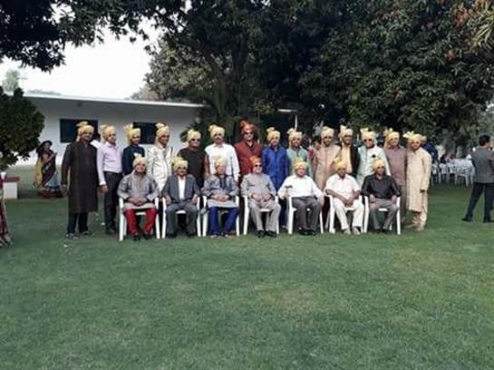 Men wearing traditional attire and turbans gather for a cultural celebration in a garden.