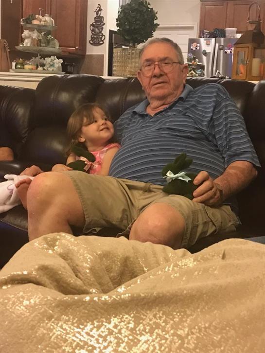A grandfather and granddaughter share a cozy, smiling moment on the couch.