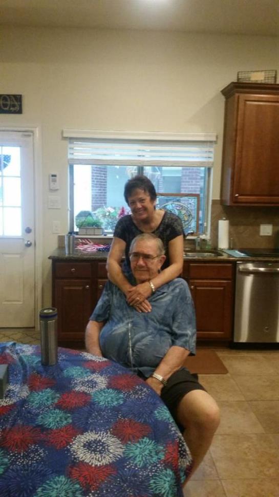 A woman lovingly embraces a man from behind in a warm kitchen atmosphere.