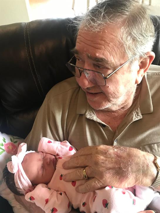 Elderly man enjoys quality time holding his newborn granddaughter at home.