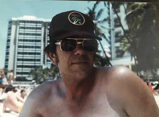 A man enjoys a sunny day at the beach, surrounded by palm trees and modern buildings.