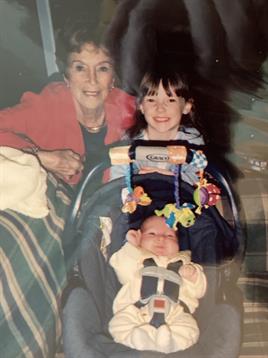 A grandmother smiles joyfully while holding her grandchildren in a warm, inviting living room.