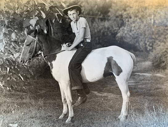A young cowboy sits on a white horse with black patches, enjoying a peaceful outdoor moment.