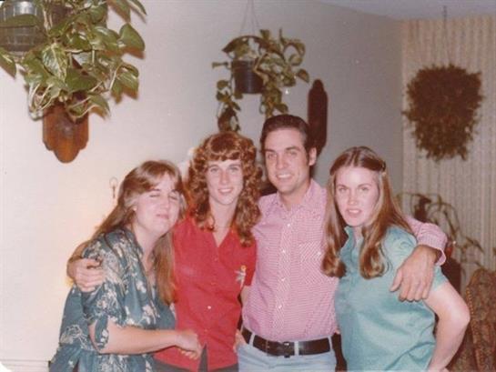 Four friends enjoy a relaxed gathering, smiling and posing with plants in the background.