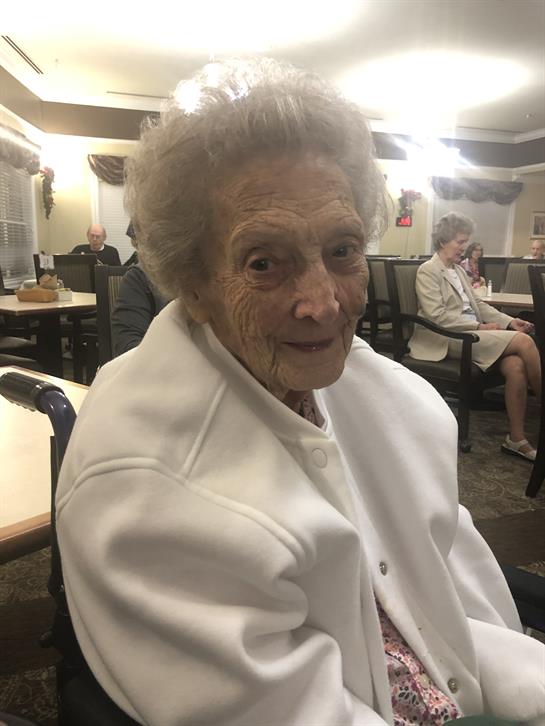 An elderly woman with gray hair enjoys a cozy afternoon with friends in a community living room.