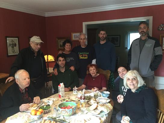 A group enjoys a meal together at a table filled with food and drinks in a cozy home.