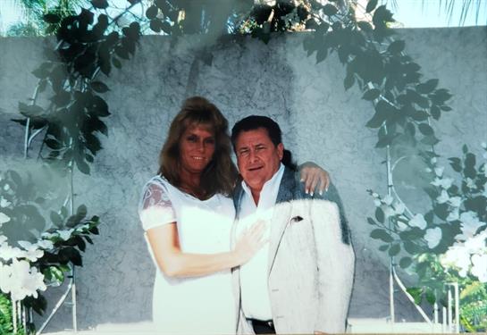 A couple stands together, embracing in a joyful moment, framed by lush foliage at an event.