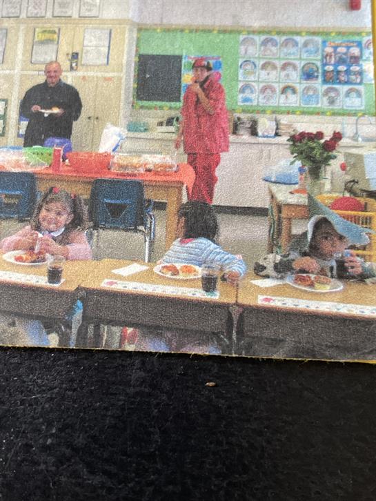 Kids are seated at tables eating lunch while a teacher supervises the fun atmosphere.