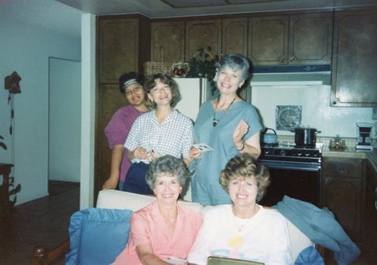 A group of five women smiles and enjoys each other's company in a cheerful kitchen.