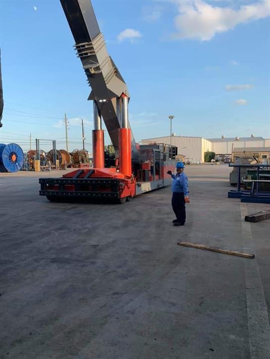 Machinery operator guides large equipment in an industrial yard under a blue sky.