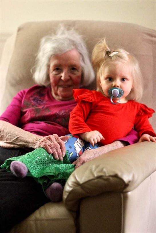 An elderly woman and a young girl relax together on a cozy sofa, sharing a moment of affection.