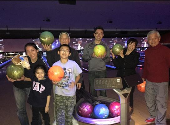 A group of six people, including children, smiles and holds bowling balls in a local bowling alley.