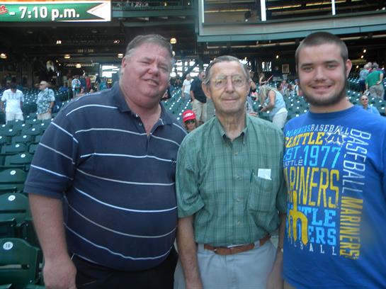 Three men smile and stand together, enjoying a lively atmosphere at a sports event.
