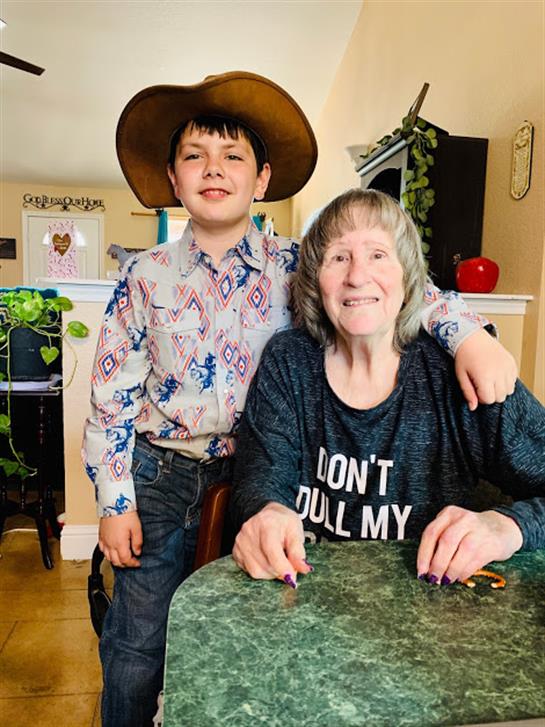 A boy in a cowboy hat smiles with an older woman at a dining table, enjoying their time.