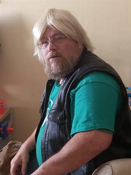 A man with long blonde hair and a beard sits casually in a room with relaxed expression.