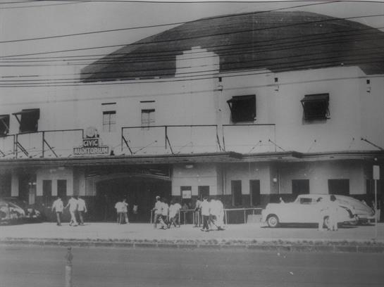 Busy street scene with groups of people outside a historic building during the day.