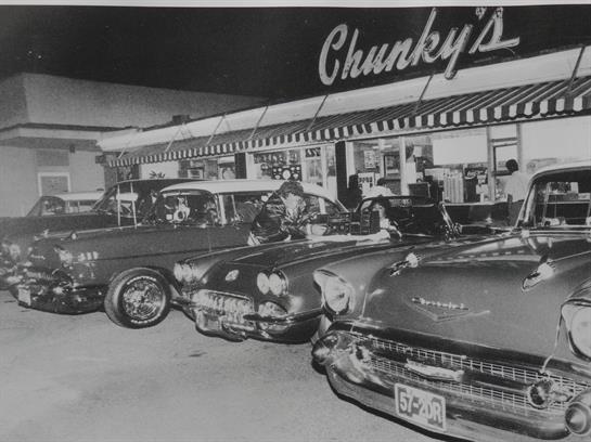 Classic cars gather at a nostalgic diner during a vibrant night, showcasing automotive history.