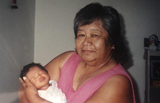 An elderly woman smiles, cradling her newborn grandchild, highlighting family love.