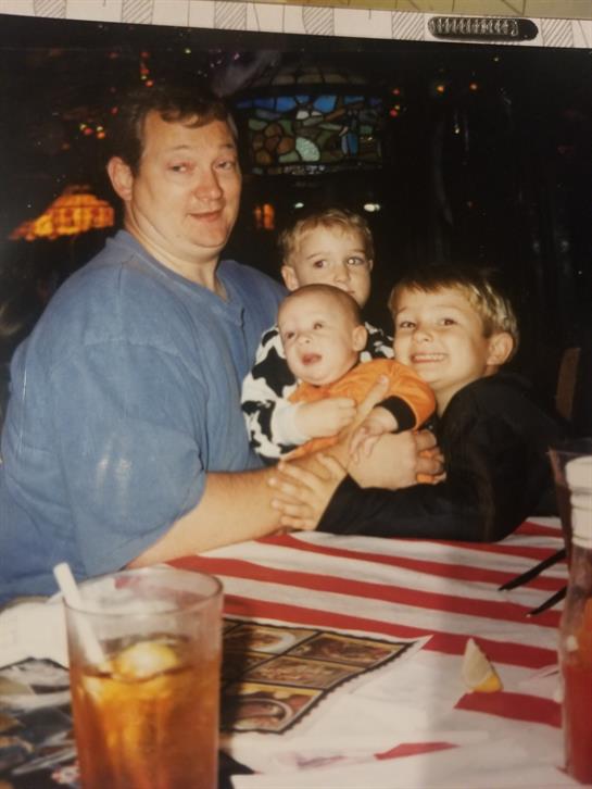 A man joyfully holds a baby while three children gather around him in a cheerful atmosphere.