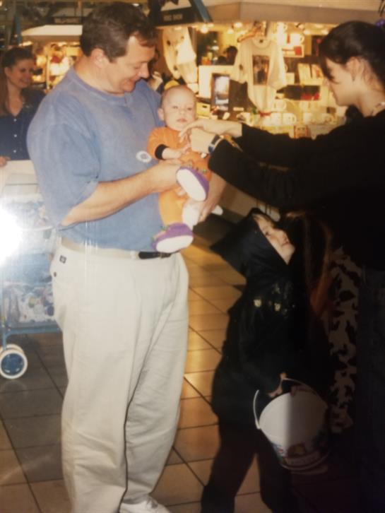 A father holds a baby while a child engages with the baby, creating a warm family moment.