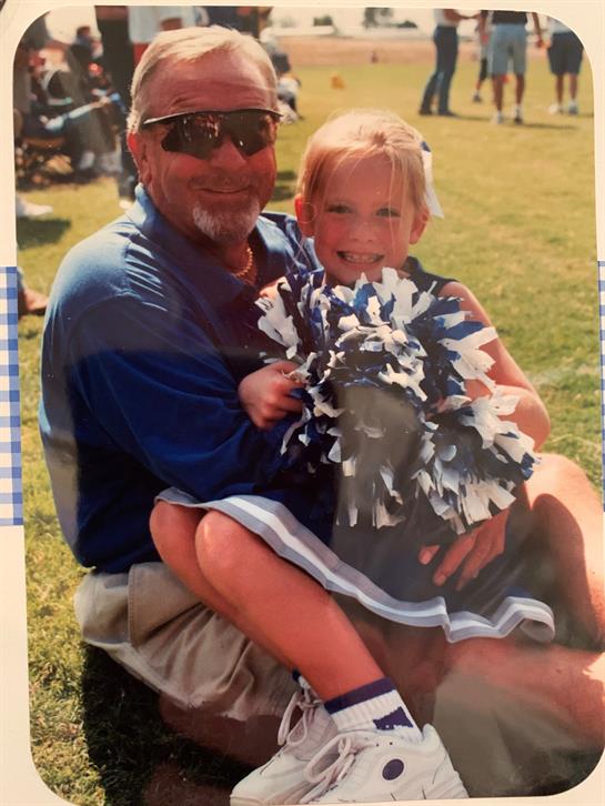 Grandfather and granddaughter share a joyful moment at a sunny sports gathering in the park.