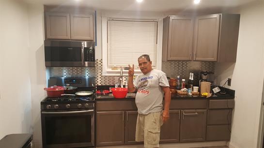 A man stands in a well-equipped kitchen, casually cooking and enjoying the moment.
