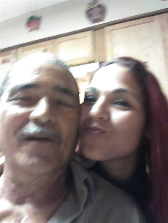 A young woman playfully kisses an older man in a warm, inviting room filled with laughter.