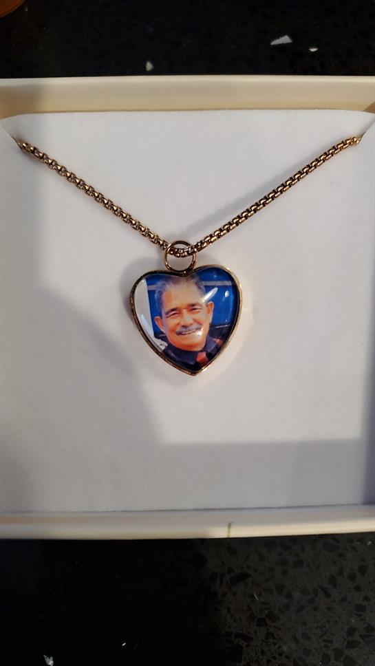 A heart-shaped pendant hangs from a chain, displaying a smiling man's photo, perfect for keepsakes.