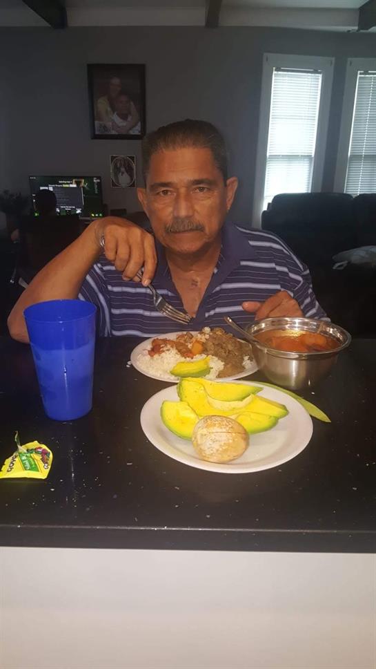 A man is sitting at a table, enjoying a meal of rice, beans, and fresh fruit in his home.