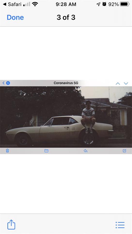 A man casually sits on the roof of a vintage car parked outside a home in a calm suburb.