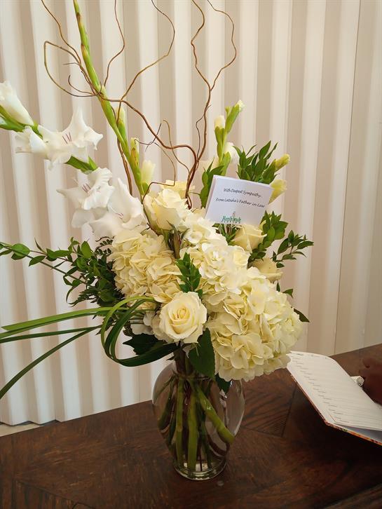 A stunning white flower arrangement featuring roses and orchids graces a wooden table with elegance.