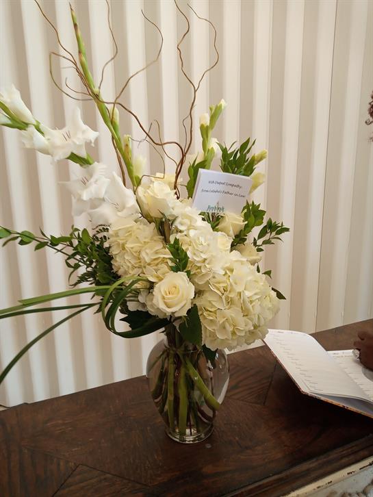 Beautiful floral display featuring white roses, orchids, and greenery in a vase on a table.