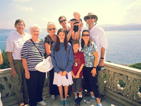 Family and children pose together at a coastal viewpoint with water in the background.