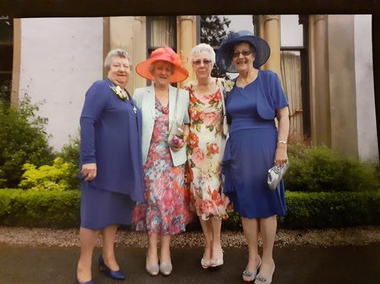 Women dressed in vibrant outfits pose together outside a garden venue, smiling joyfully.