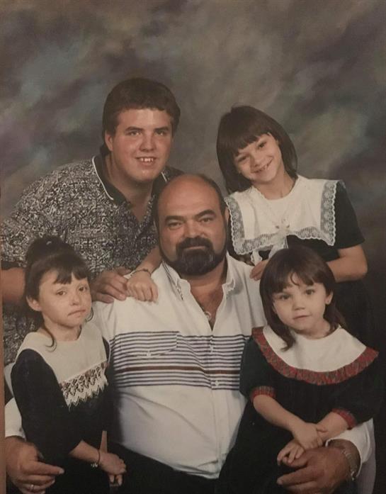 Group of four young girls and two adult males pose together with smiles in a studio setting.