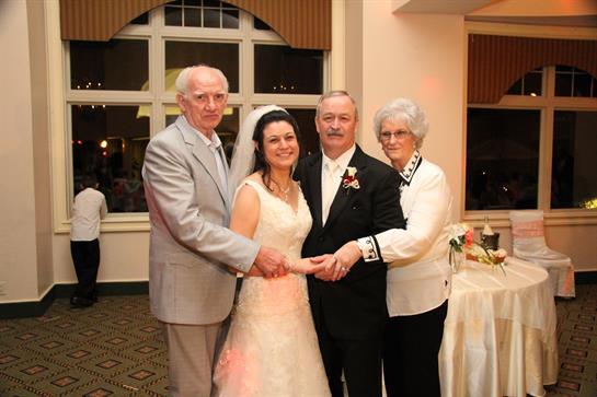 A bride stands between her grandparents and groom at a joyous evening wedding gathering.