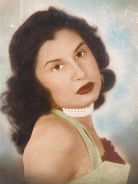 Woman with dark, wavy hair poses gracefully in a vintage outfit showcasing classic beauty.