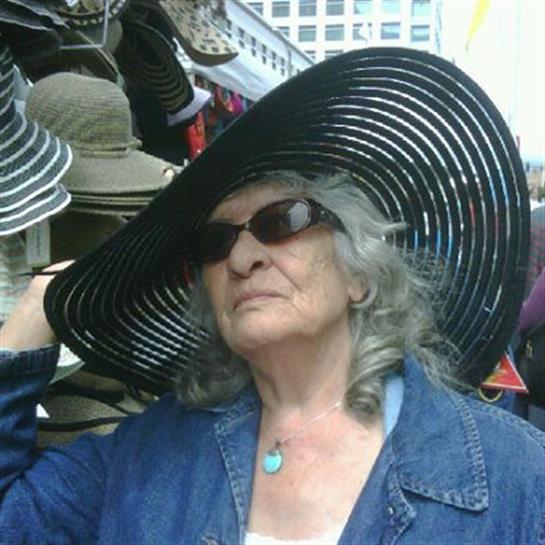 Woman with gray hair and sunglasses enjoys shopping at a vibrant outdoor market.