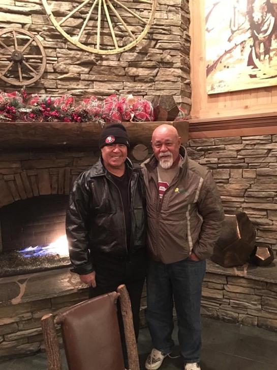 Two friends smile by a warm fireplace in a cozy, winter-decorated mountain lodge.