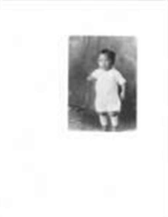 A young child confidently wears a simple white dress, embodying innocent early childhood charm.