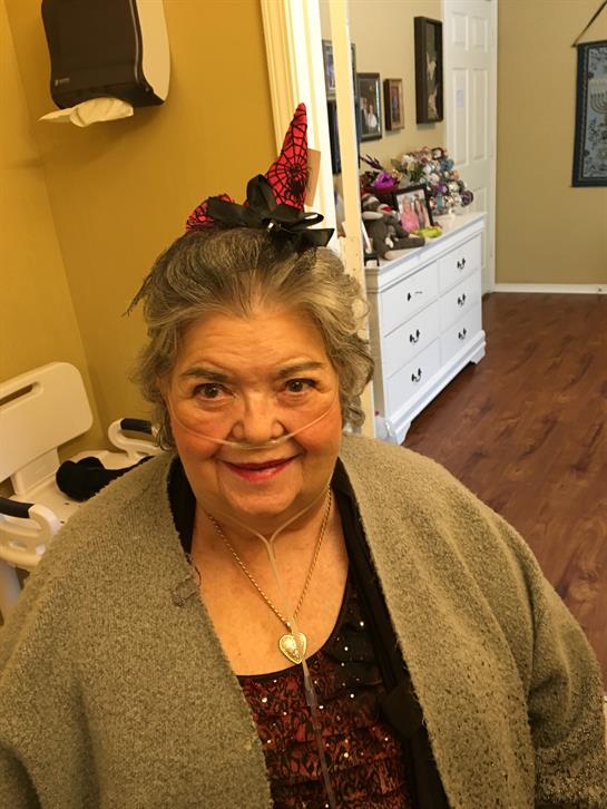 An older woman in festive attire smiles warmly in a cheerful living room with family.