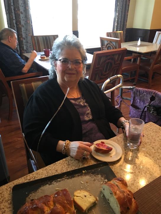 A senior woman smiles while savoring a slice of dessert, seated in a welcoming cafe atmosphere.