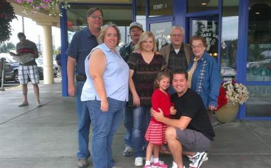 A happy family poses outside a shop, smiling and enjoying a warm moment together.