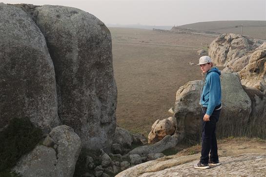 A boy stands on rocky ground, overlooking a vast, fog-covered landscape with distant hills.