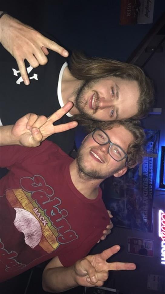 Two friends pose together, smiling and showing peace signs in a vibrant nightlife setting.